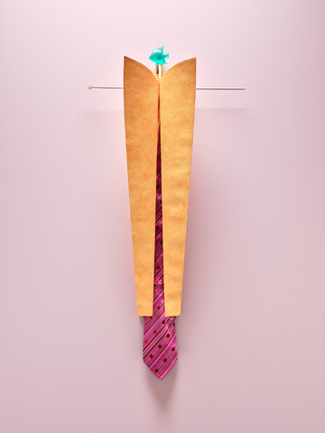 Georges J. Ayrault, **From A.**, 2025.
A striped tie with various patterns, suspended by a needle from a bunch of 
mismatched knitting needles (gift from Martine who knits and sews a lot) in 
a prototype of a tie rack made from folded wallpaper, peach–terracotta 
color, 2000s, held by hair clips, with a green fish-shaped doorknob found 
in Bergerac whose sky-blue–violet pair is hidden in another piece, 
and a small scrap of wrapping paper.
Photo ©Nicolas Lafon - © Photo &copy;Nicolas Lafon, Paris Internationale